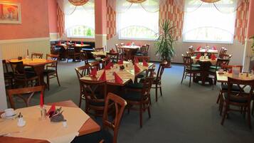 A restaurant with multiple dining tables and chairs, arranged in a spacious layout with large windows allowing natural light.