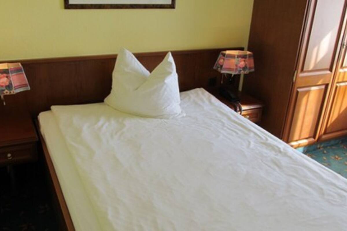 A neatly made bed with white linens and a single white pillow in a hotel room.
