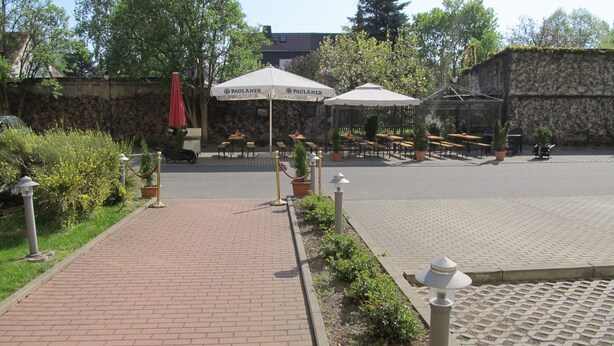 A paved outdoor area with tables and chairs, surrounded by greenery and a stone wall. - Brandiser Parkhotel (Brandis)