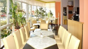 A dining area with a large table and chairs, surrounded by large windows with plants. - Brandiser Parkhotel (Brandis)