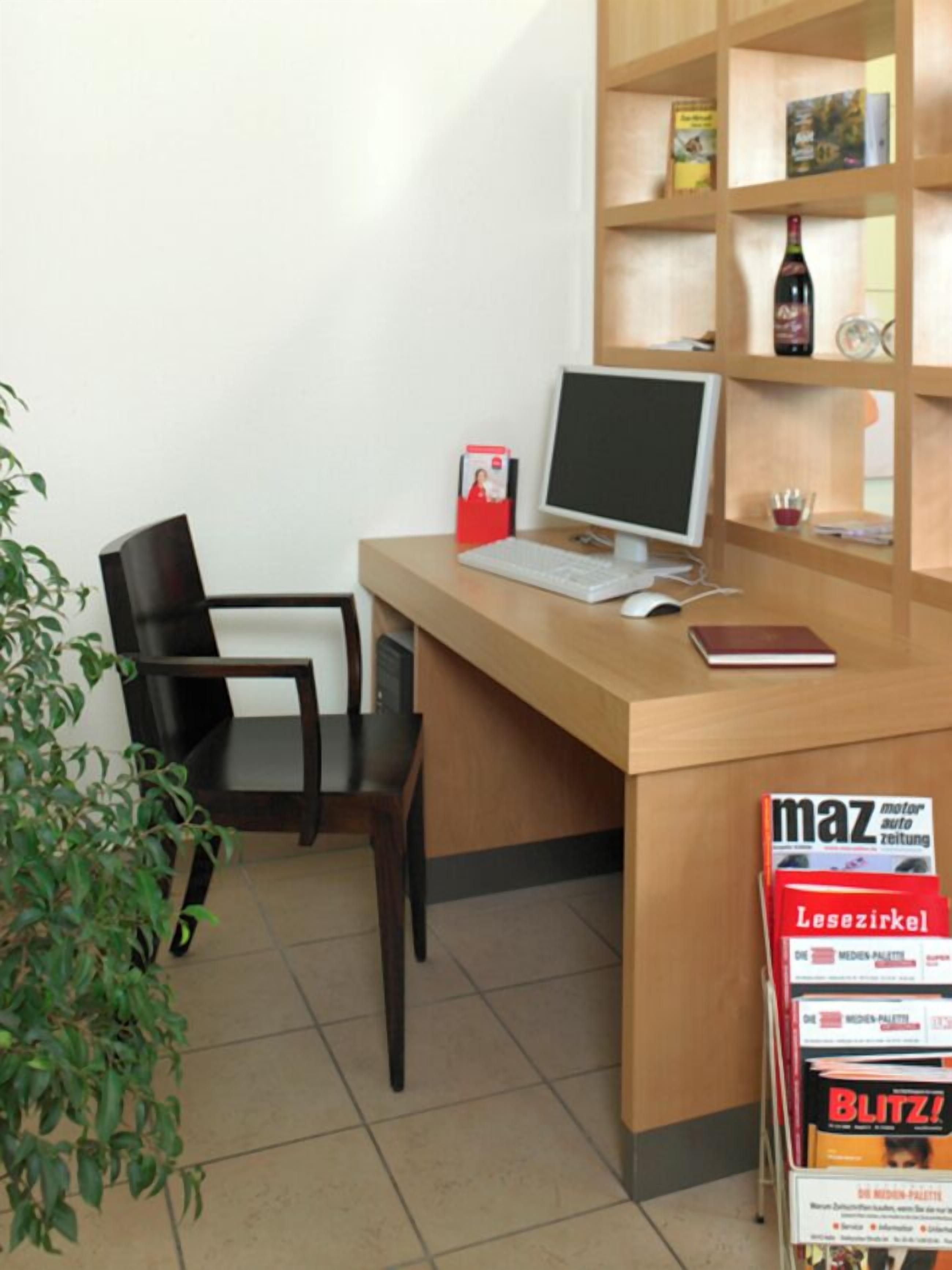 A reception desk with a computer, a chair, a small plant, and a magazine rack with 'maz' magazine.
