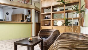 A room with a dining area, a wicker sofa, a small table, and a wooden cabinet with shelves. - ibis Leipzig Nord Ost (Taucha)