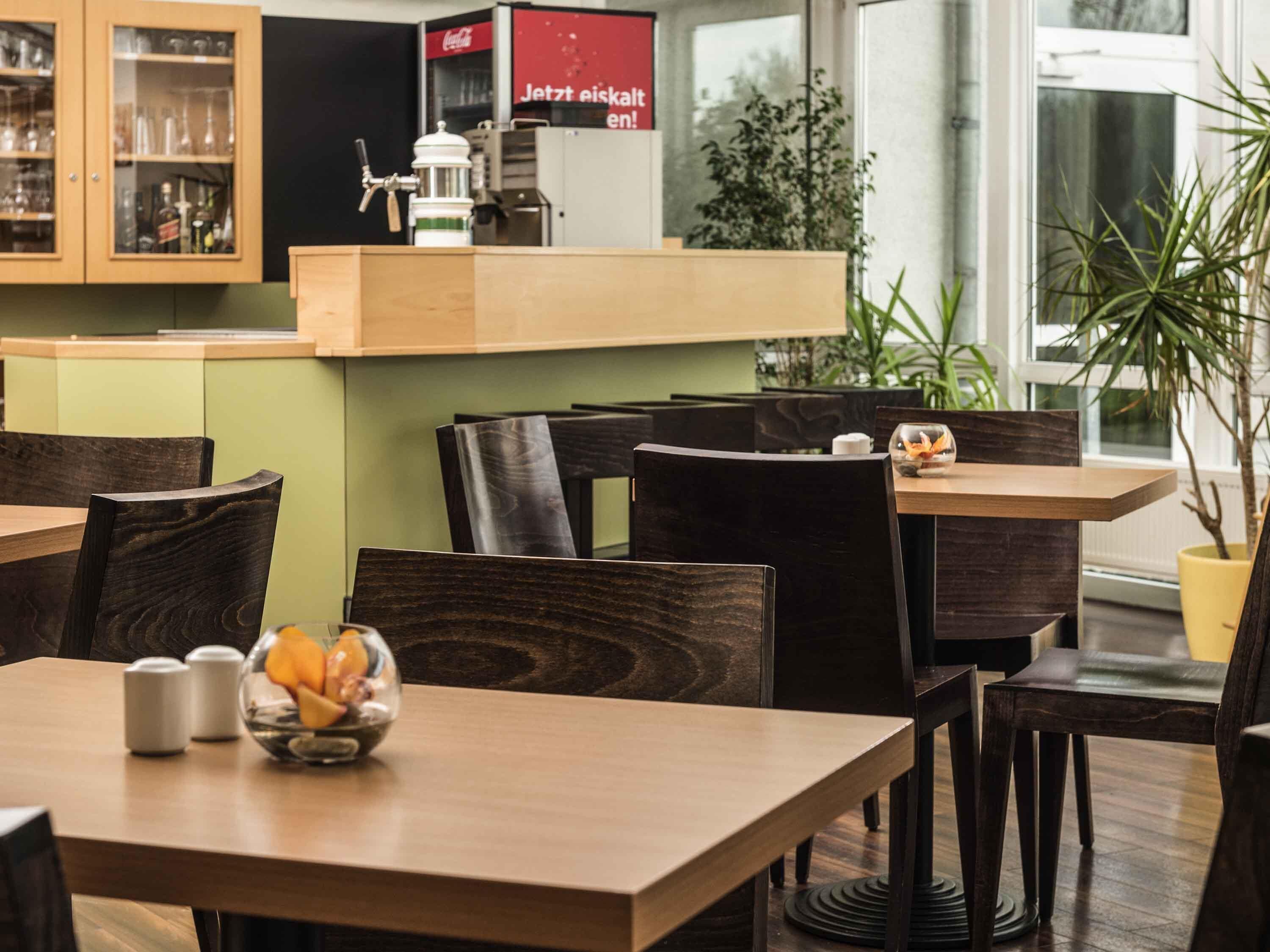 Interior de restaurante con mesas y sillas de madera, una máquina de café y un refrigerador de Coca-Cola.