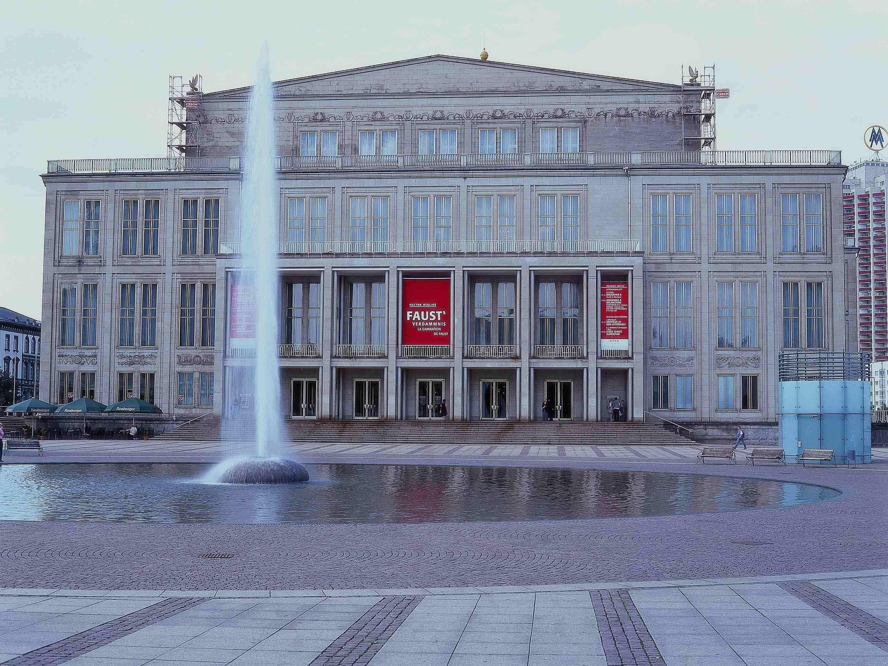 A large building with a fountain in front, multiple windows, and red banners.