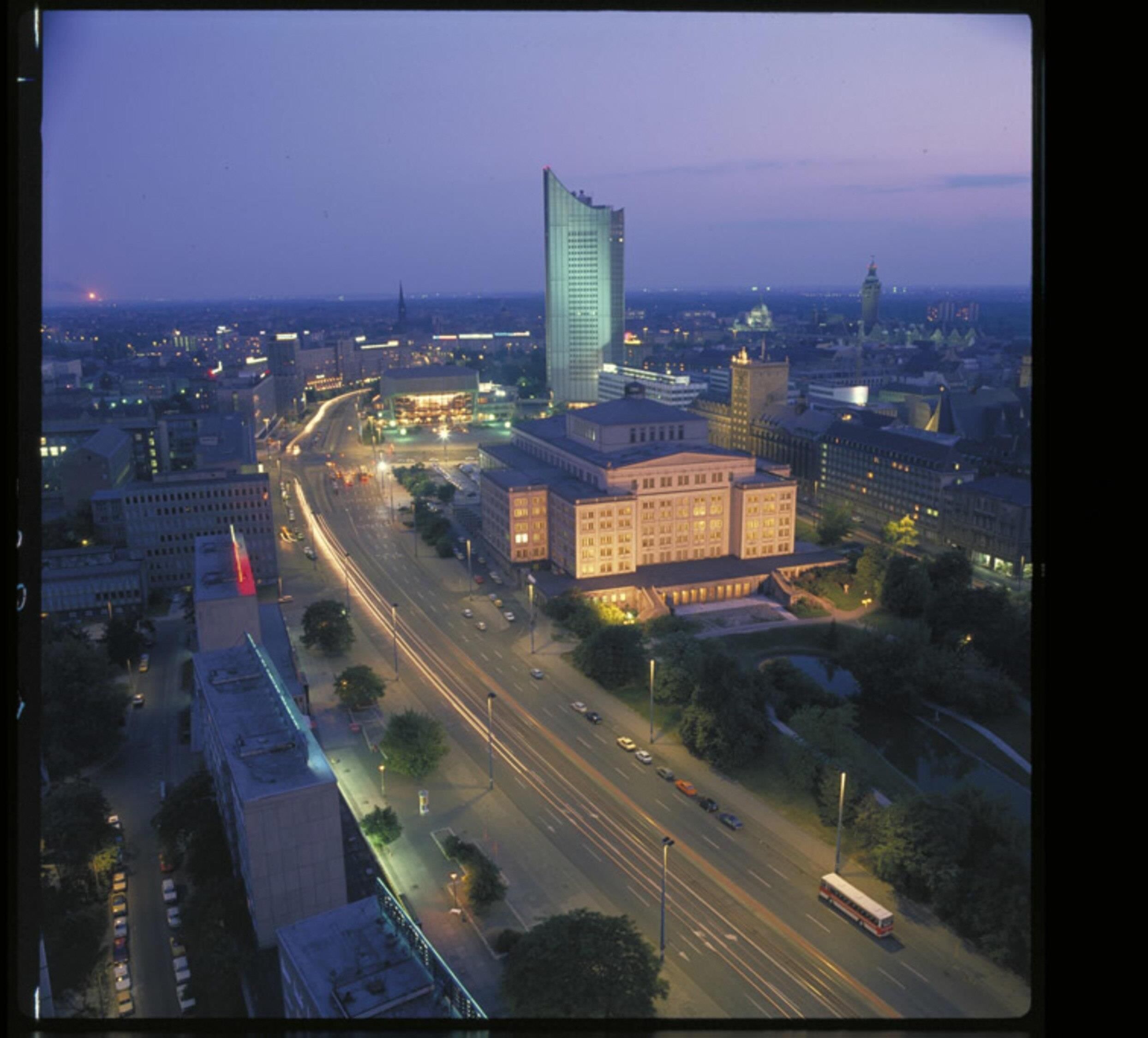 A cityscape at dusk with a prominent modern building, wide roads, and a mix of commercial and institutional buildings.