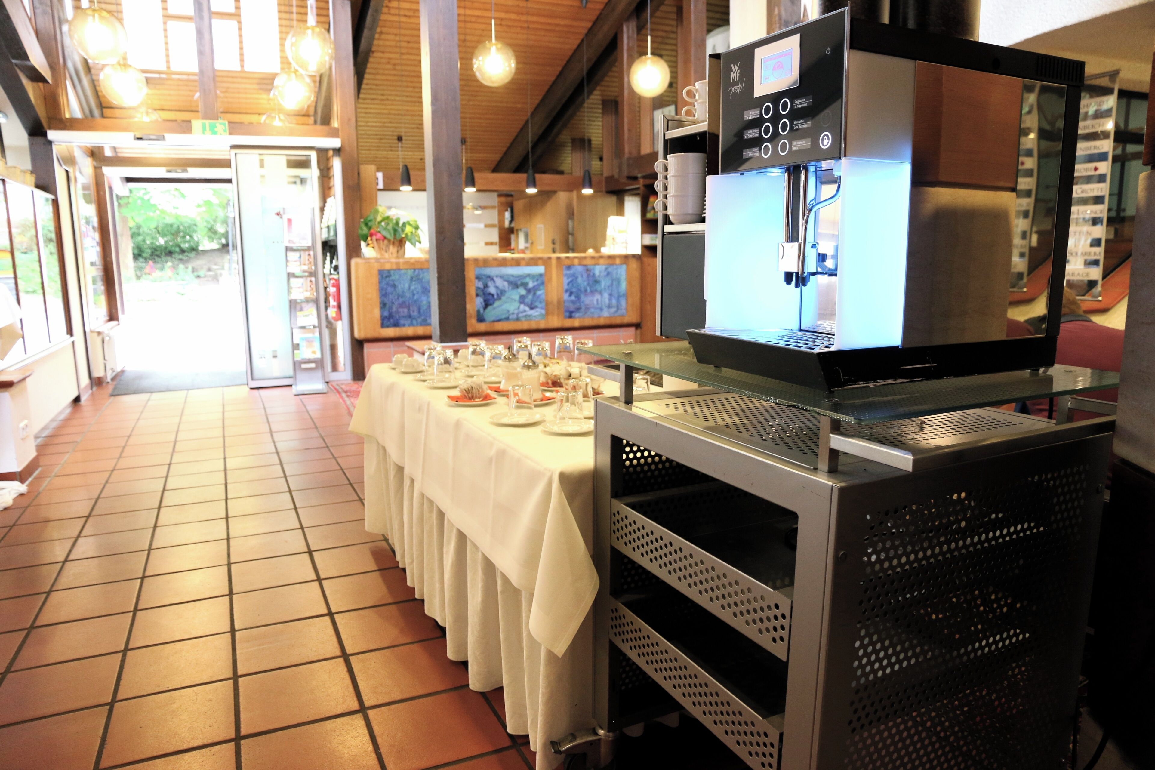 Ein Restaurant mit einem langen Tisch, der für eine Mahlzeit gedeckt ist, einer Kaffeemaschine und einem Fliesenboden.
