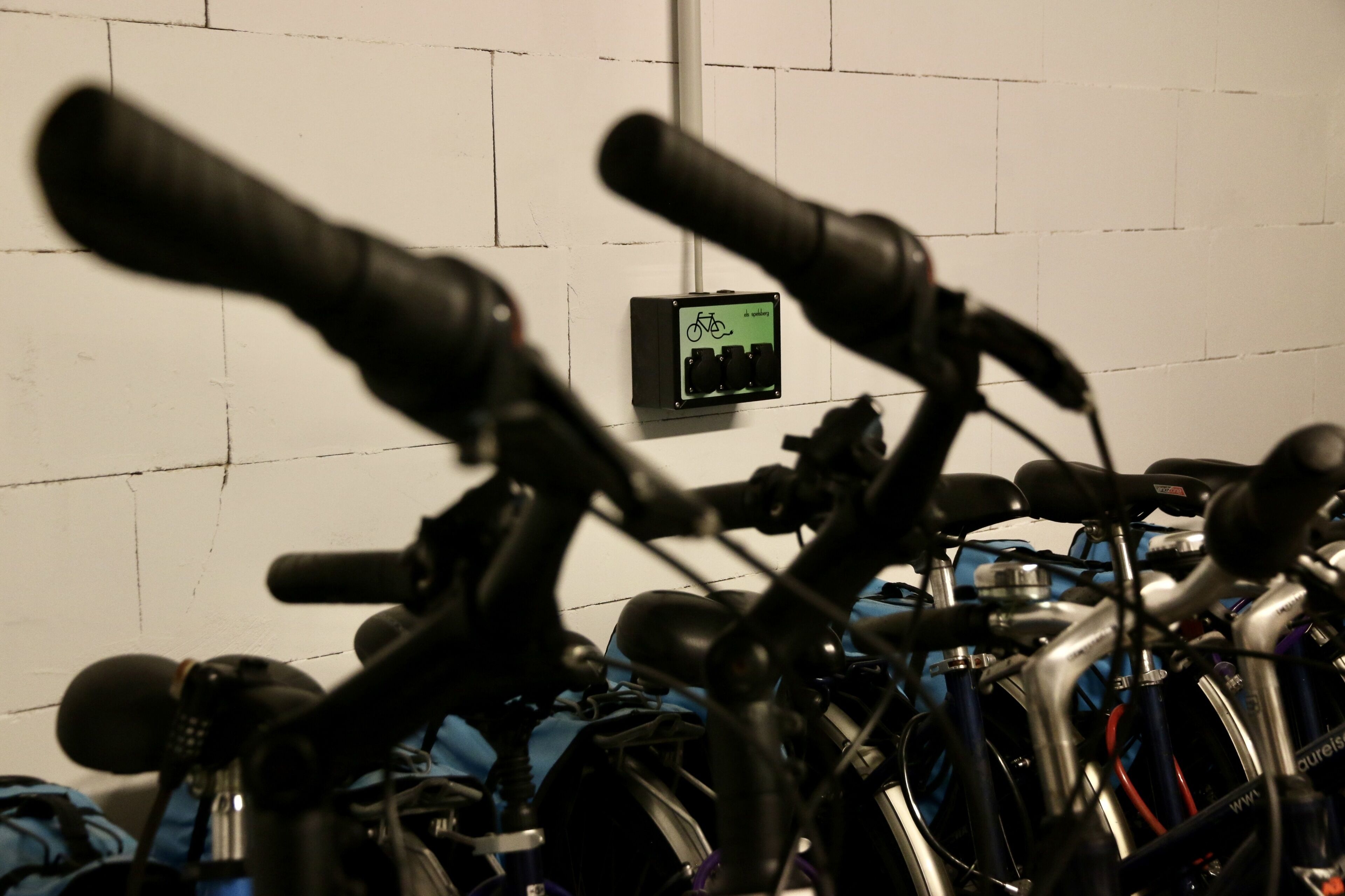 A row of bicycles parked in a garage with a bike charging station in the background.