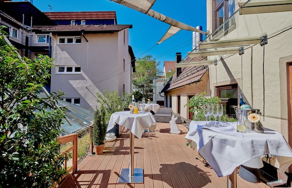 Un patio con mesas dispuestas para comer, rodeado de edificios y vegetación.