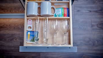 A drawer with two white mugs, three clear wine glasses, and various food items including chocolate bars and a box of peppermints.
