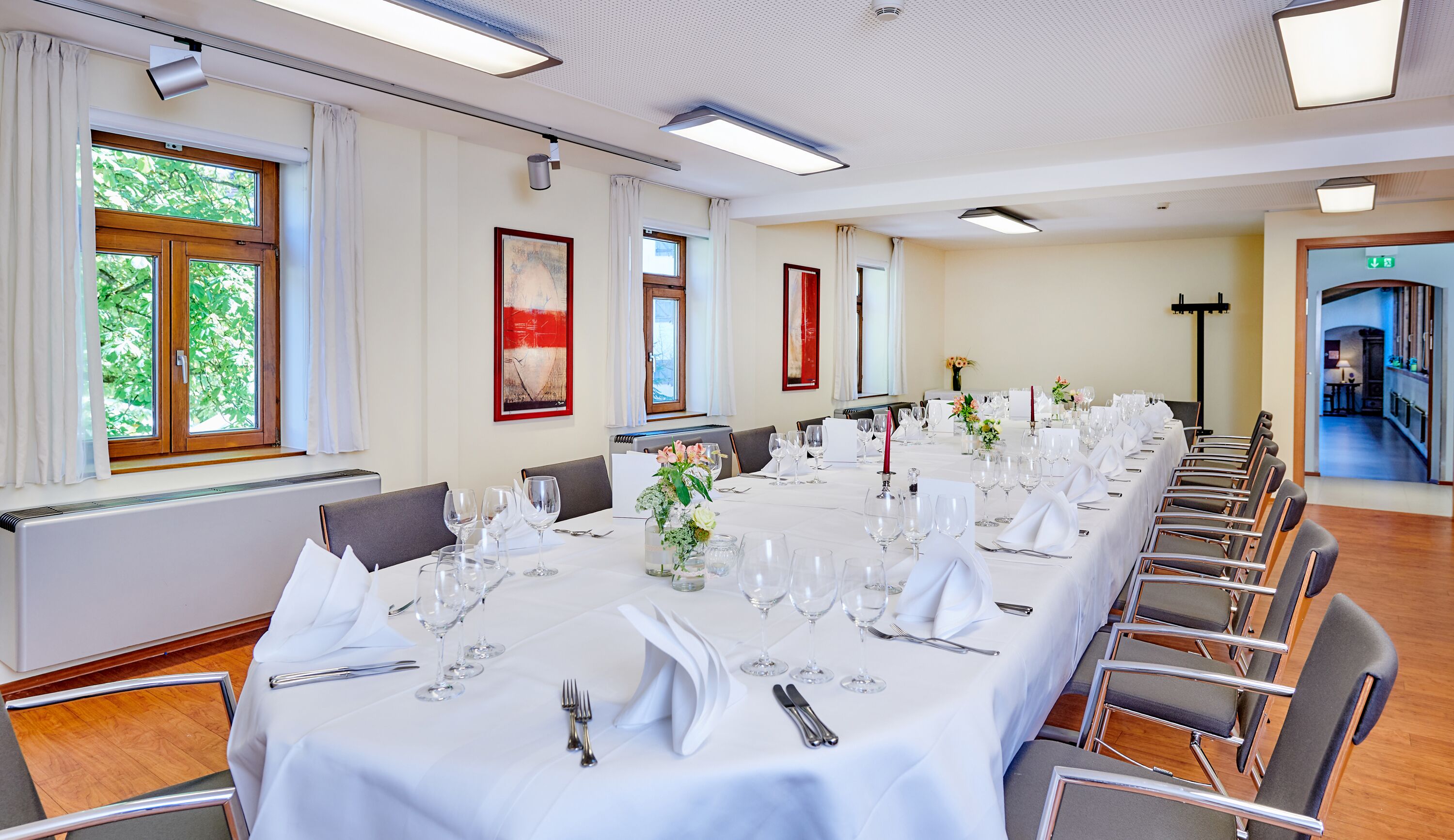 Un salón de conferencias con una larga mesa dispuesta para un evento formal, equipado con sillas, mesas y cristalería.