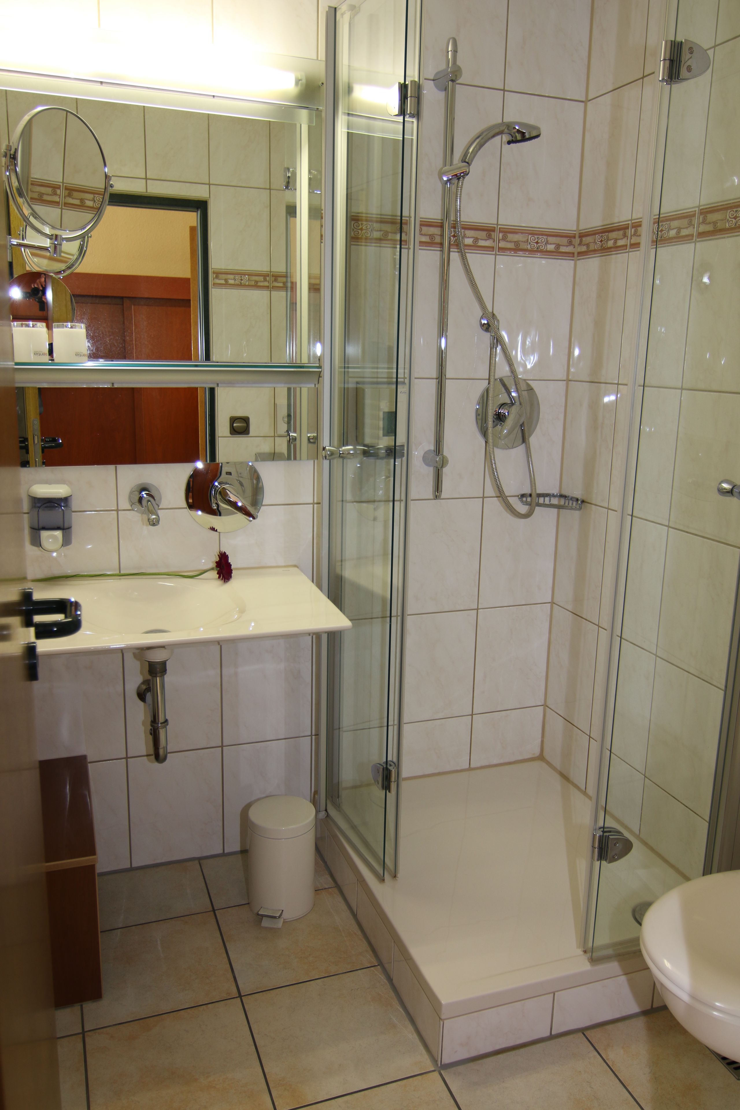 Ein Badezimmer mit einer Duschkabine, einem Waschbecken inklusive Spiegel und einer Toilette.
