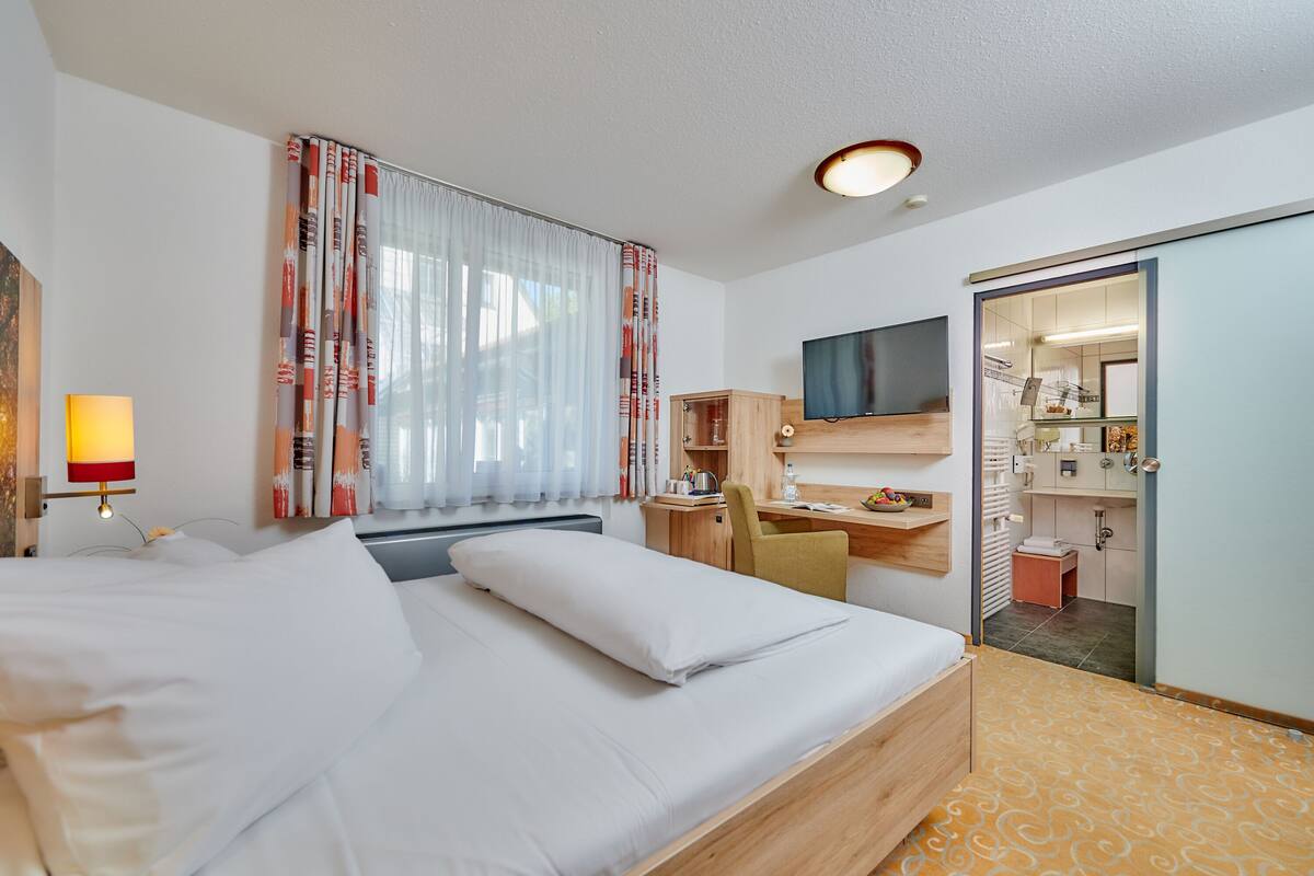 Een hotelkamer met een bed, bureau, stoel, televisie en een badkamer die door een geopende deur zichtbaar is.