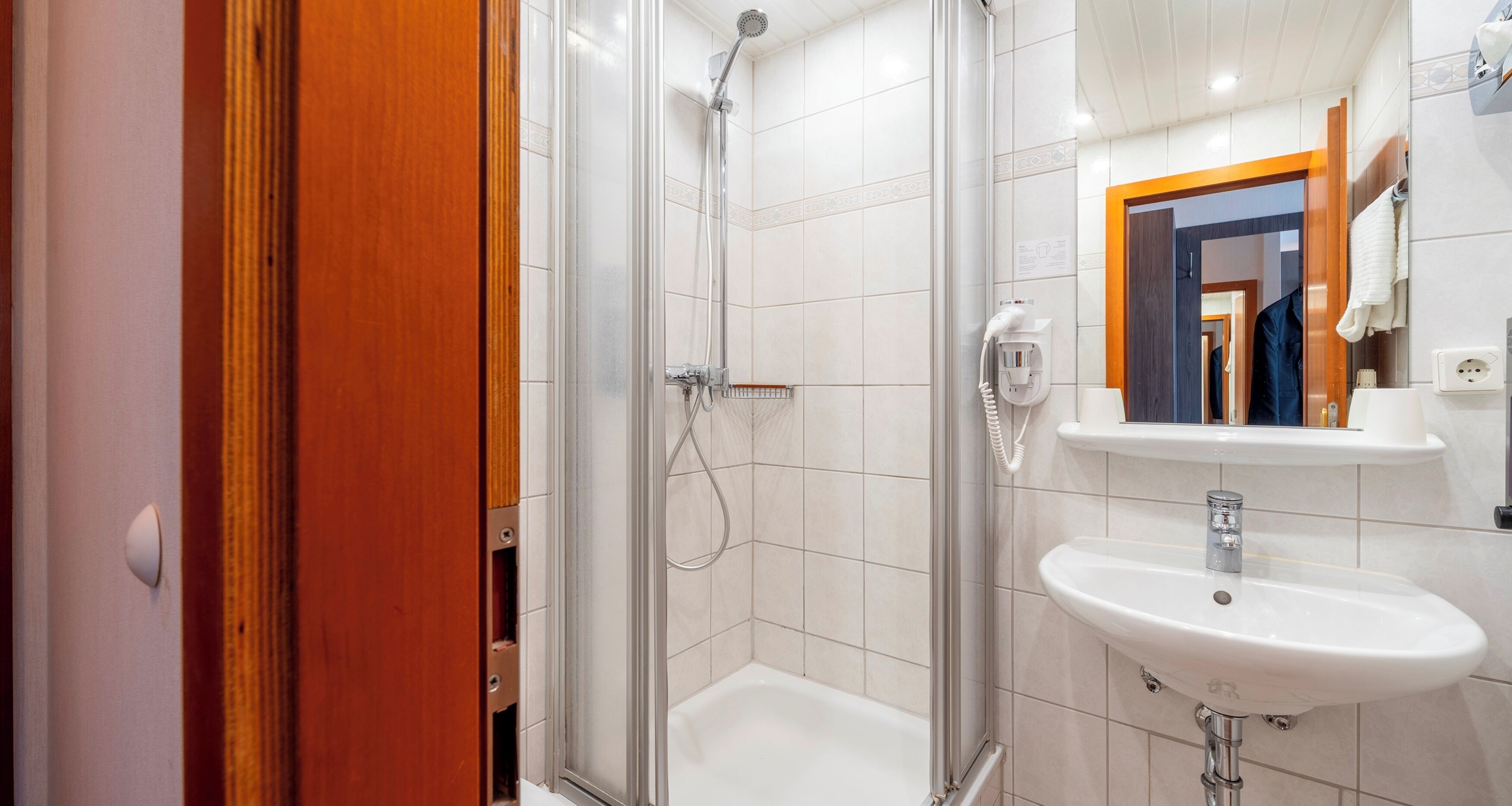 Ein modernes Badezimmer mit einer Duschkabine aus Glas, einem weißen Waschbecken und einem Spiegel darüber.
