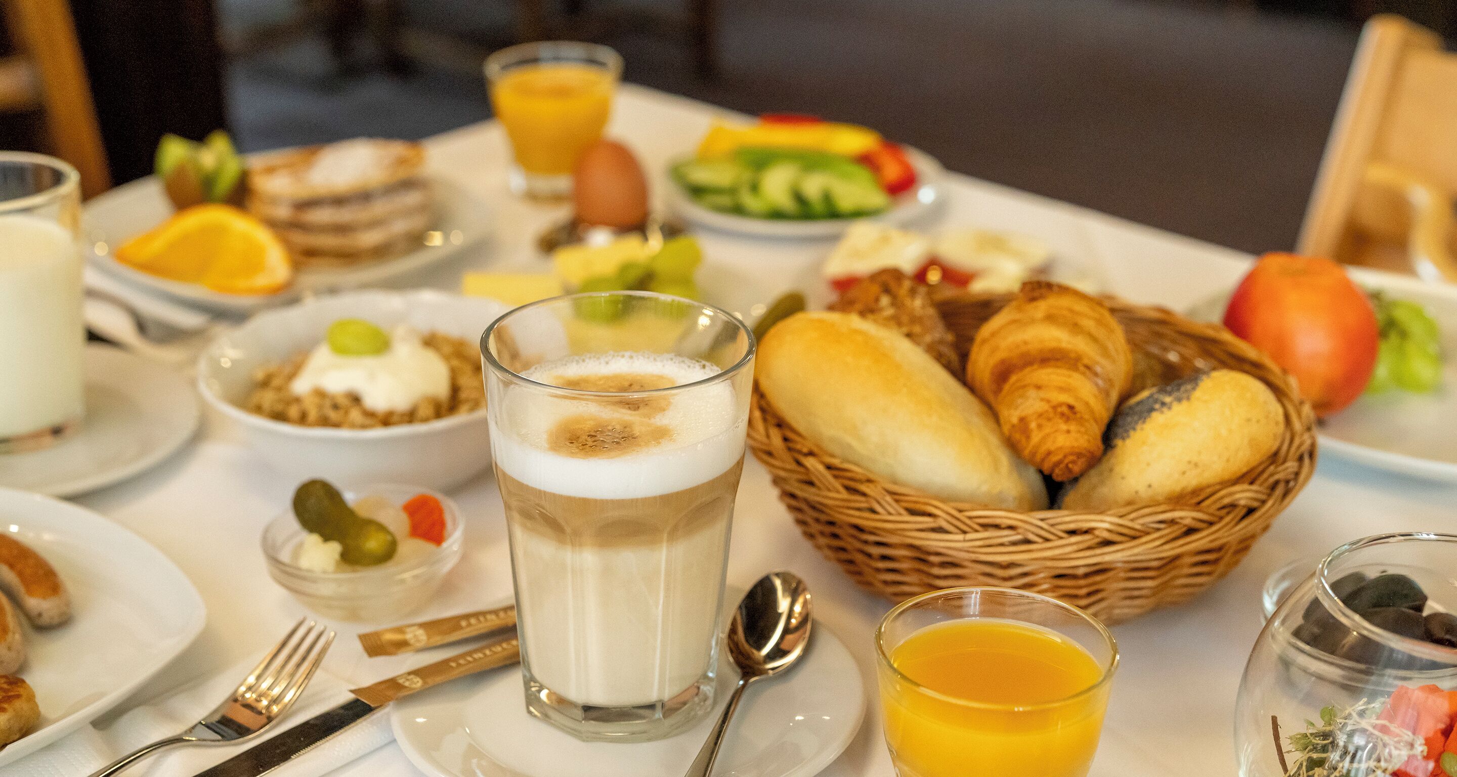 A breakfast table with various food items, including croissants, fruits, and beverages.