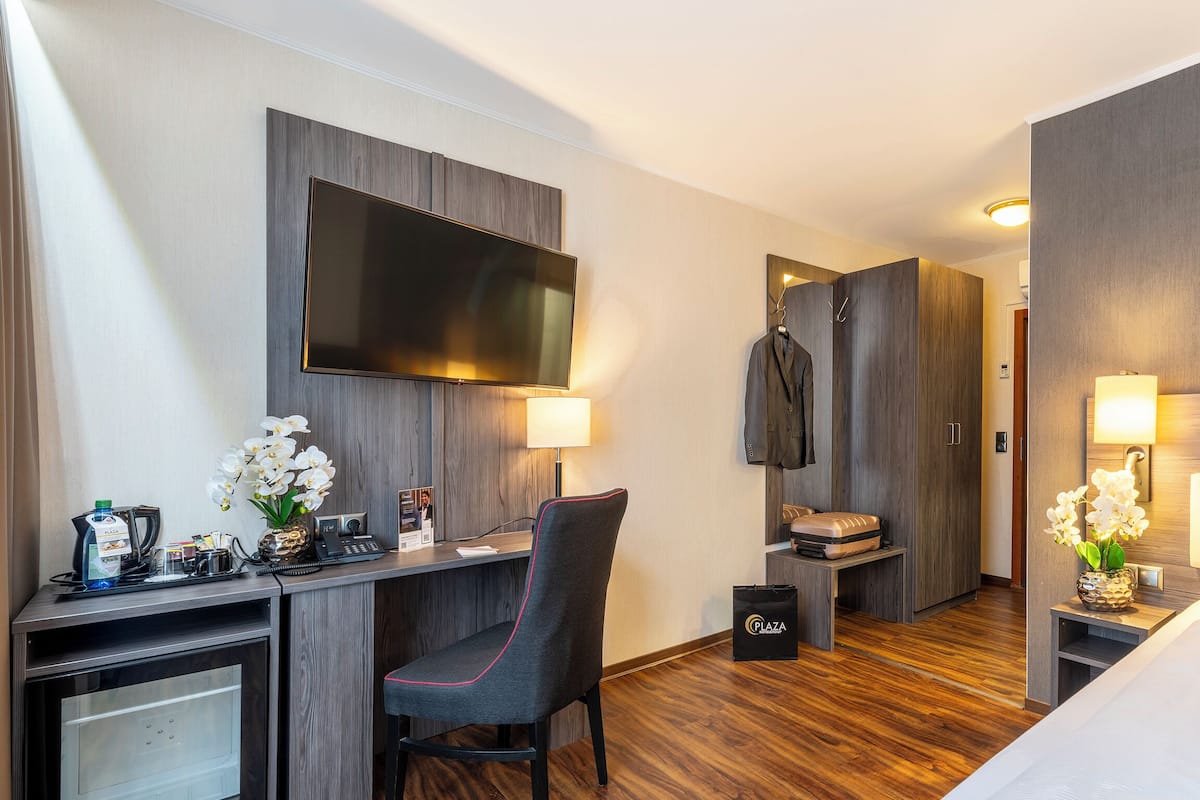 A hotel room with a bed, desk, chair, TV, and a minibar.