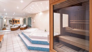 A modern spa with two large tubs, a wooden sauna, and a seating area with a bench.
