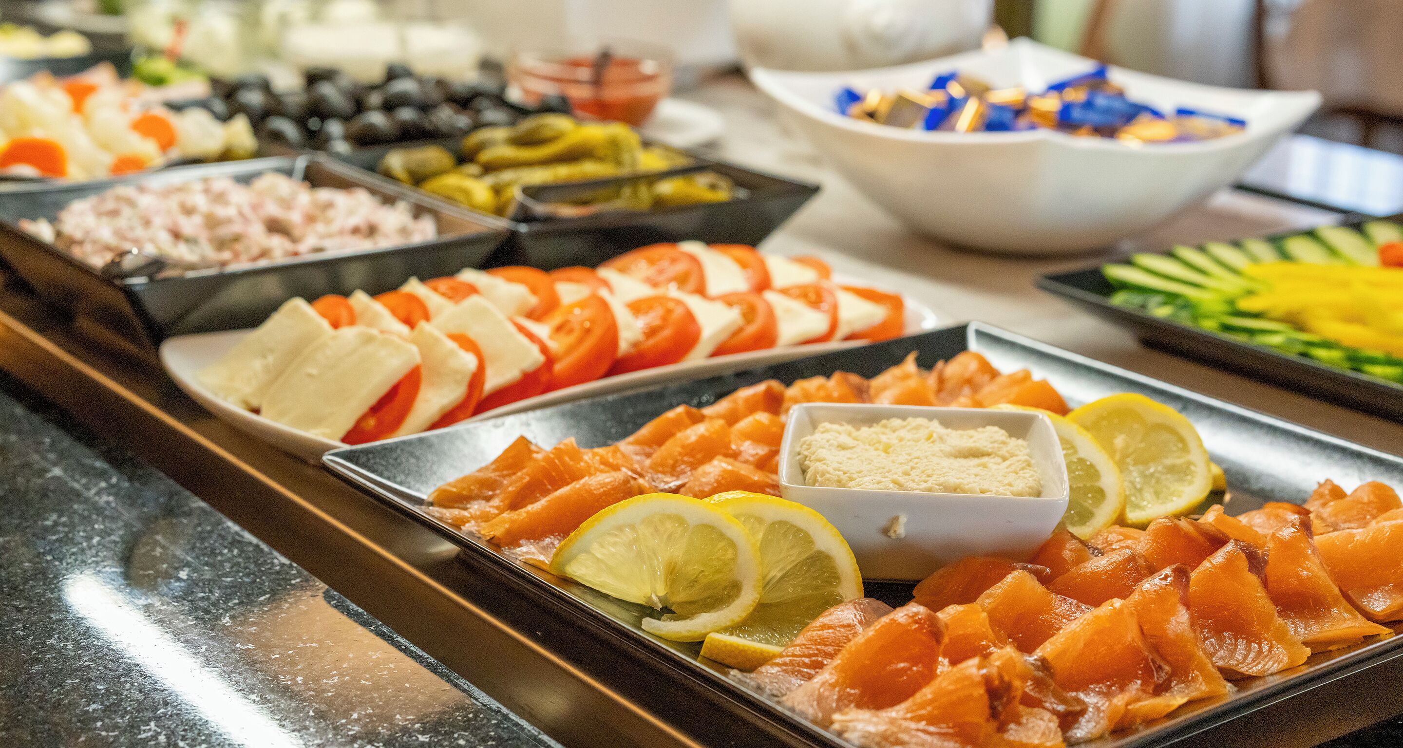A buffet with various food items including salmon, cheese, and vegetables.