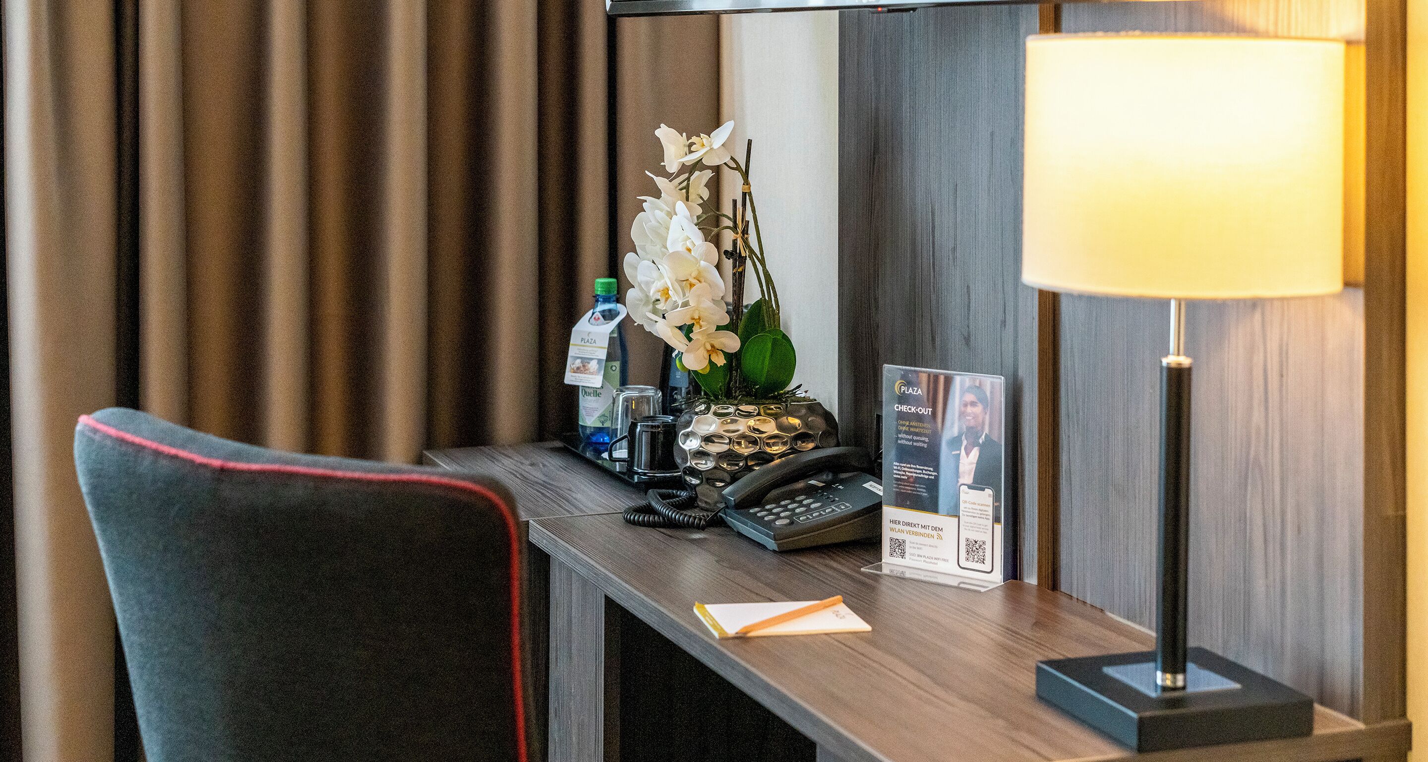 Mostrador de recepción de hotel con teléfono, expositor de folletos, botella de agua y lámpara.