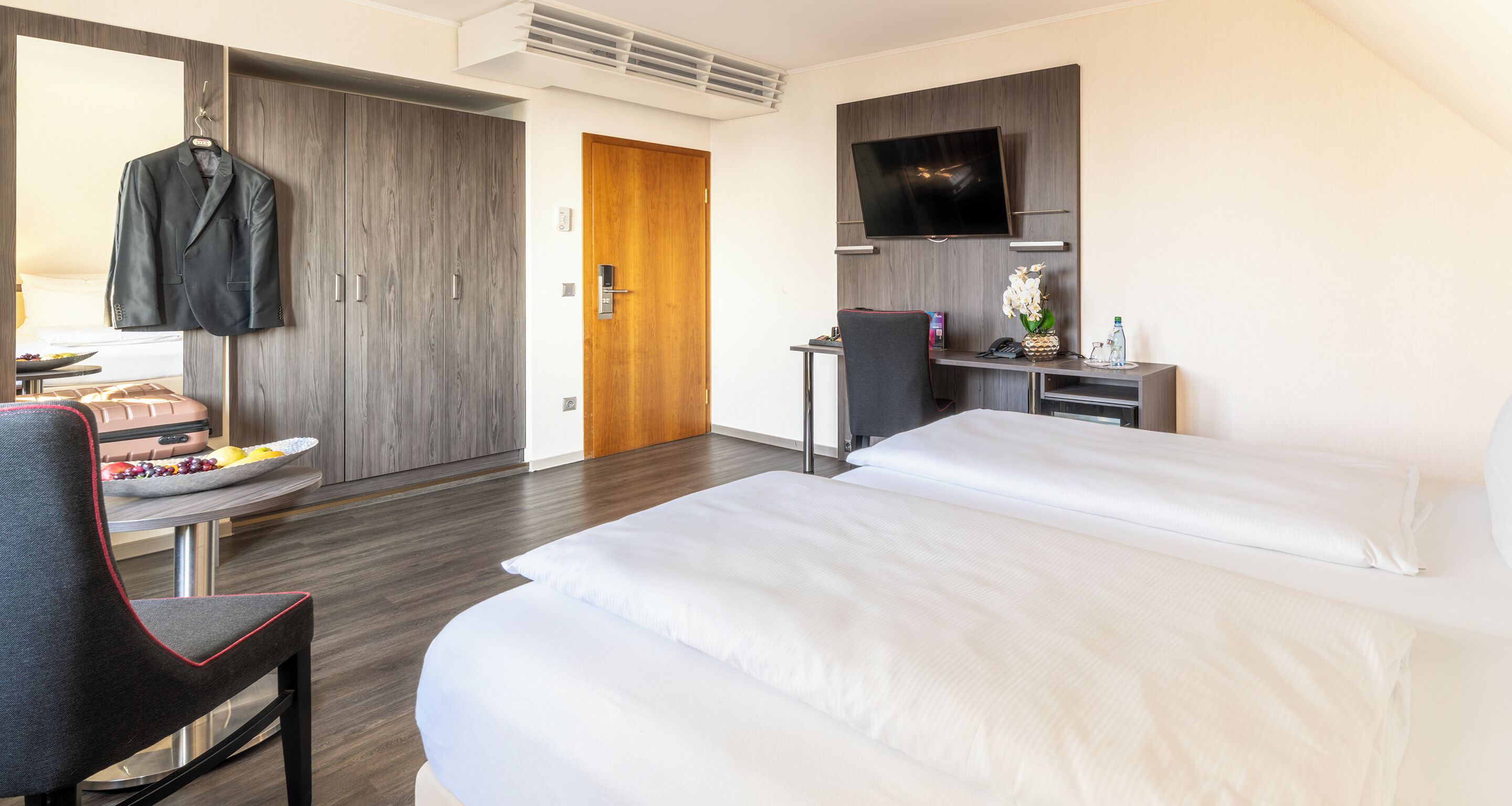 Una habitación de hotel con dos camas, un escritorio con computadora, televisión y armario.