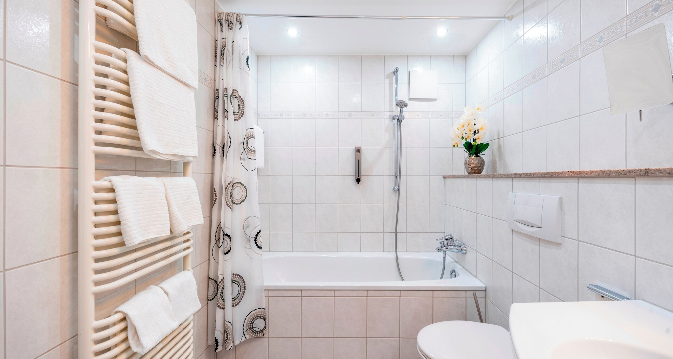 A modern bathroom with a bathtub, toilet, and a towel rack with folded towels.