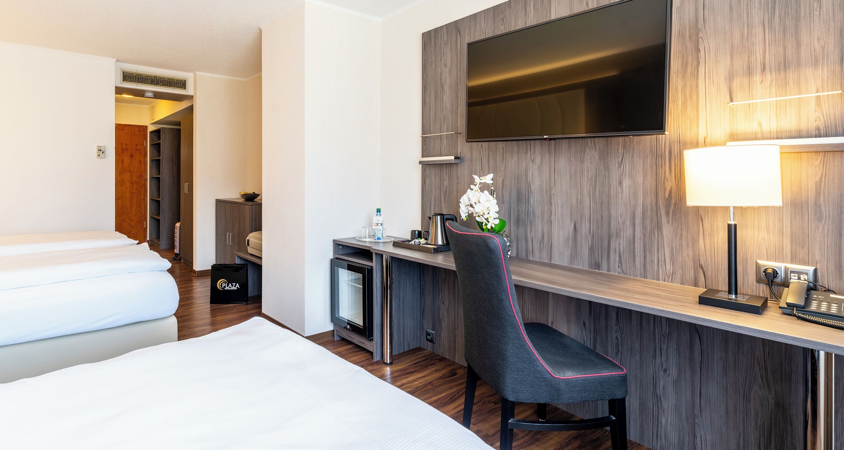 Una habitación de hotel con cama, escritorio, silla, televisor y lámpara.