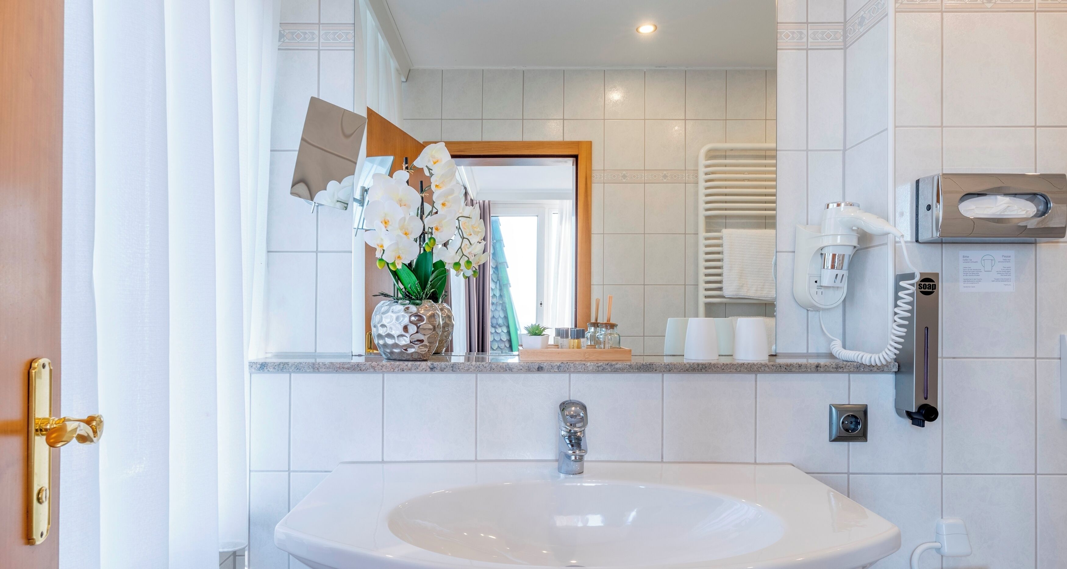 A bathroom with a white sink, a mirror, a towel rack, a soap dispenser, and a telephone.