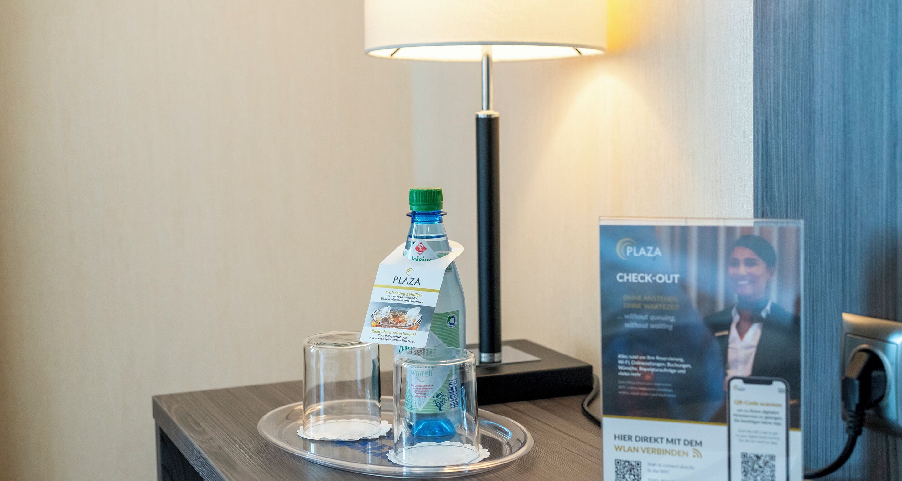 A hotel room with a minibar, a lamp, and a sign for check-out services.