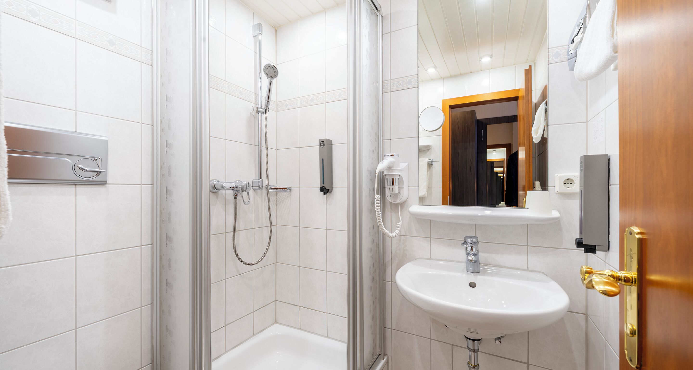 Ein modernes Badezimmer mit einer gläsernen Duschkabine, einem weißen Waschbecken und einer Holztür.