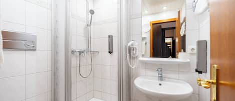 A modern bathroom with a glass-enclosed shower, a white sink, and a wooden door.