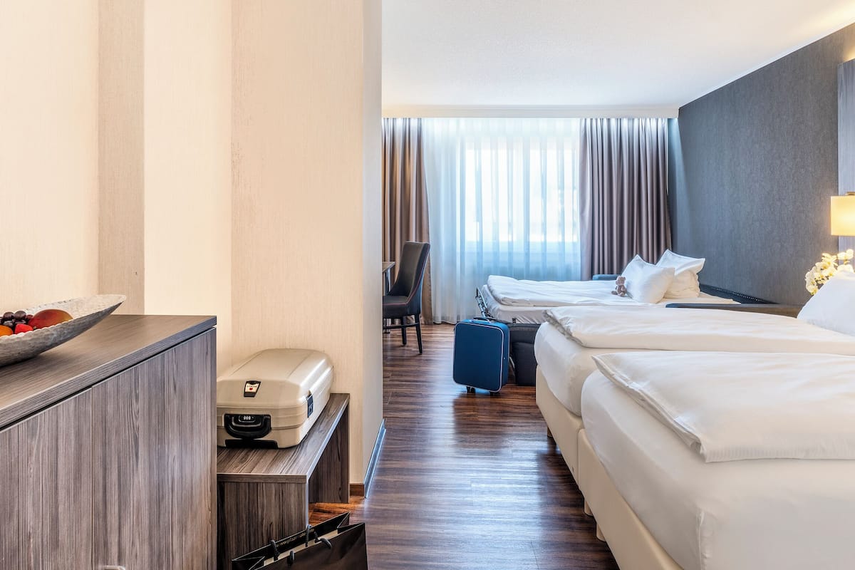 A hotel room with two beds, a desk with a printer, a bowl of fruit, and a suitcase.