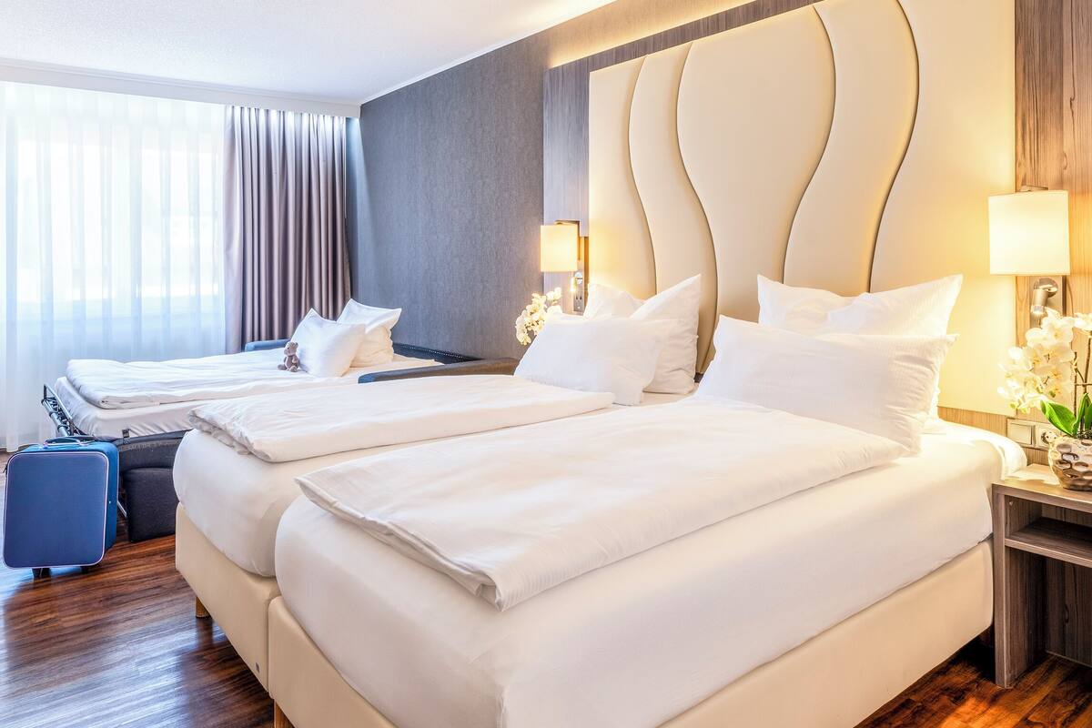 A hotel room with two beds, a chair, a desk, and a suitcase.
