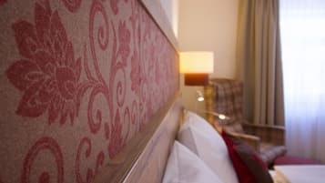 A hotel room with a patterned headboard, a lamp, a chair, and a bed with pillows.
