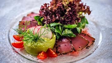 A clear glass plate with a salad consisting of greens, radishes, and slices of meat, garnished with dill.