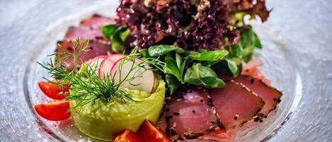 Un plato de vidrio transparente con una ensalada de hojas verdes, rábanos y láminas de carne, decorada con eneldo.