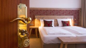 Een hotelkamer met een houten deur, een bed met witte beddengoed en een nachtkastje met een lamp.