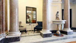 Un hall d’entrée avec un sol en marbre, un fauteuil bleu, une petite table sur laquelle est posée une plante en pot et une statue sur un piédestal.