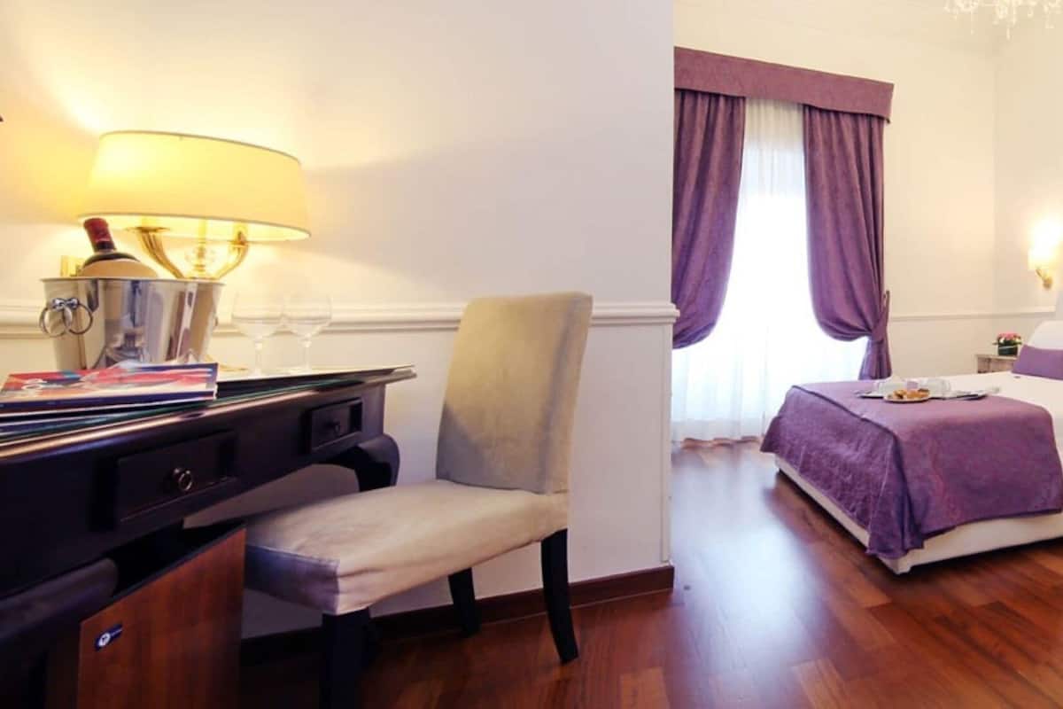 Ein Hotelzimmer mit Bett, Sessel, Schreibtisch mit Lampe und Nachttisch.
