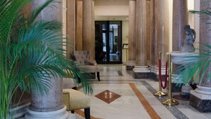 Un hall d’entrée avec des colonnes de marbre, un comptoir d’accueil et une statue.