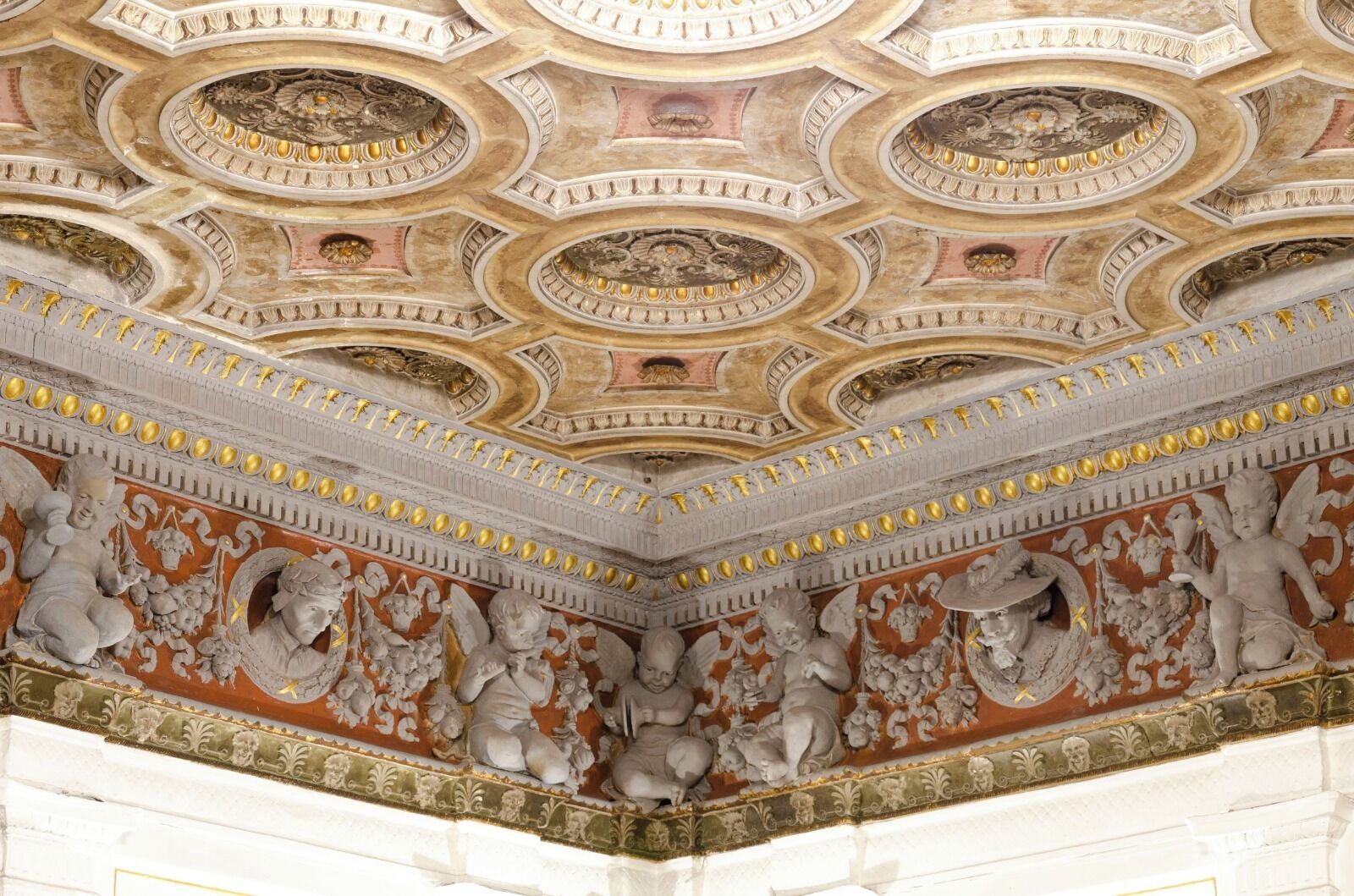 Techo con decoraciones ornamentales en dorado y blanco, incluyendo medallones circulares y esculturas en relieve.