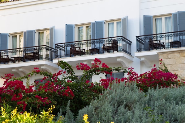A building with multiple balconies, each with a black railing and wooden chairs.