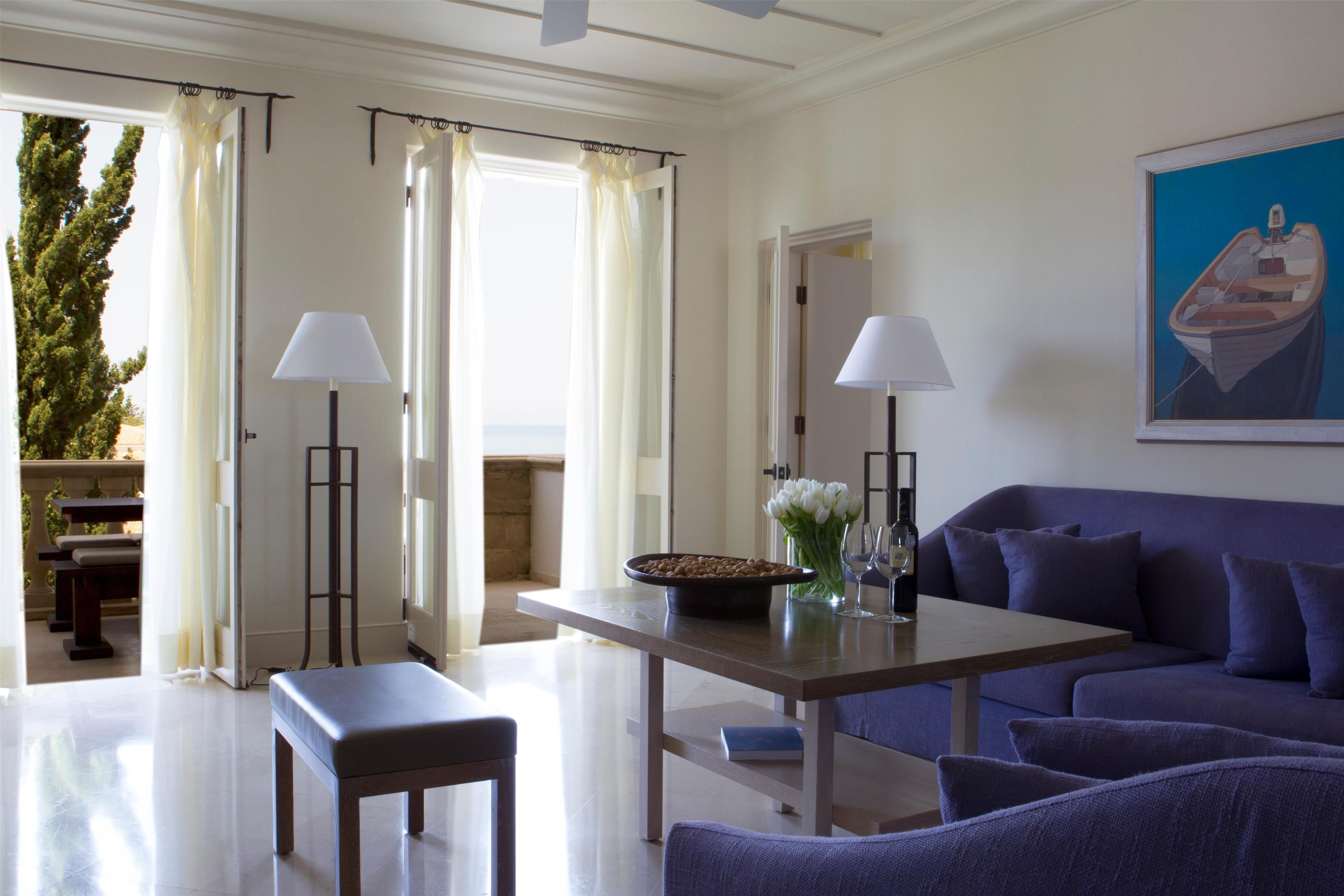 A modern living room with a sofa, a dining table, and a bench. There are two floor lamps and a painting on the wall.