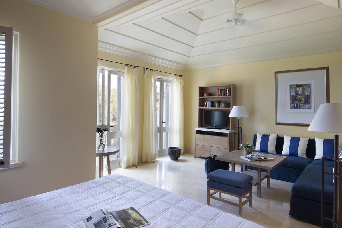 A hotel room with a bed, a sofa, a table, a TV, and a bookshelf.