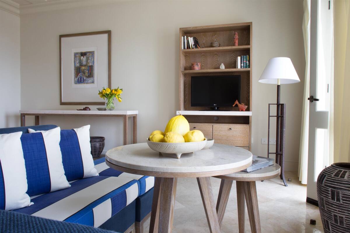 A living room with a sofa, a round table with a bowl of fruit, a TV, and a lamp.