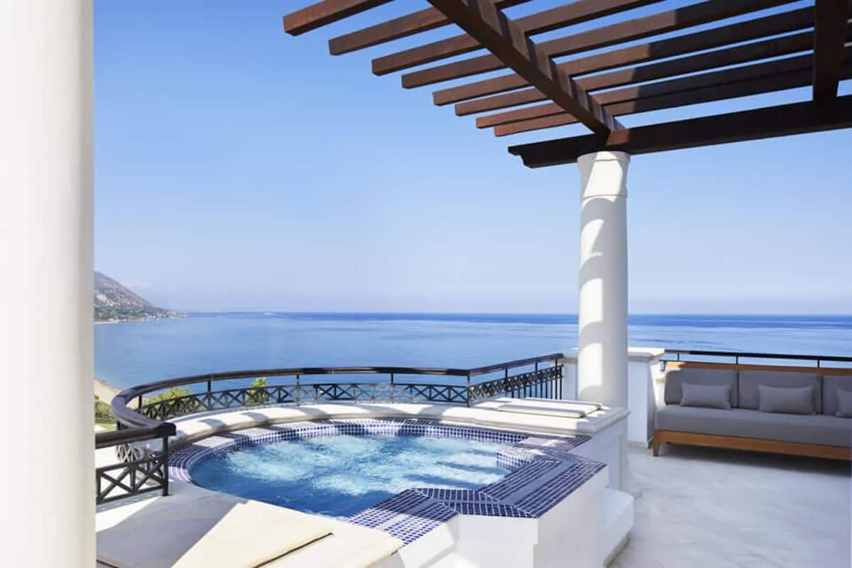 A hot tub with a view of the sea, a white outdoor sofa, and a pergola structure.