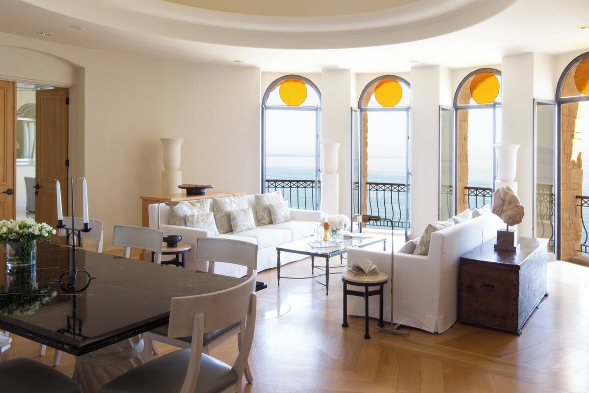 A spacious living area with a dining table, white sofas, and large windows with arched tops.