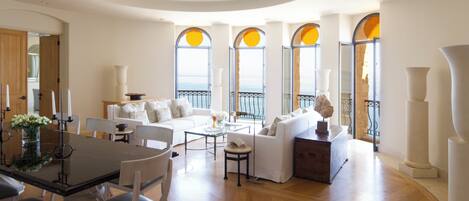 A spacious living area with a dining table, white sofas, and large windows with arched tops.