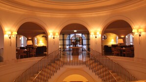 A grand interior with a central staircase, arched ceilings, and multiple seating areas. - Anassa Hotel (Neo Chorio)