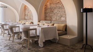 Un restaurante con mesas y sillas blancas, paredes de piedra y un ambiente iluminado por velas.