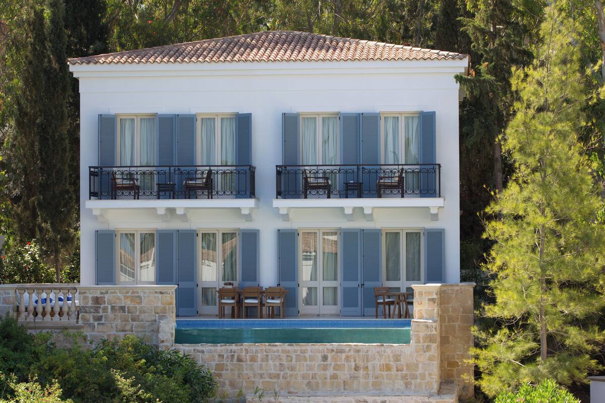 A two-story building with a swimming pool, balconies with outdoor furniture, and a stone wall.