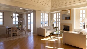 Amplia sala de estar con chimenea, comedor con mesa y sillas, y grandes ventanales con vista al mar.
